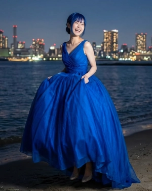 ロケーション撮影：きらめく夜景の海辺で、青いドレスと青い髪色で満面の笑みを浮かべる花嫁